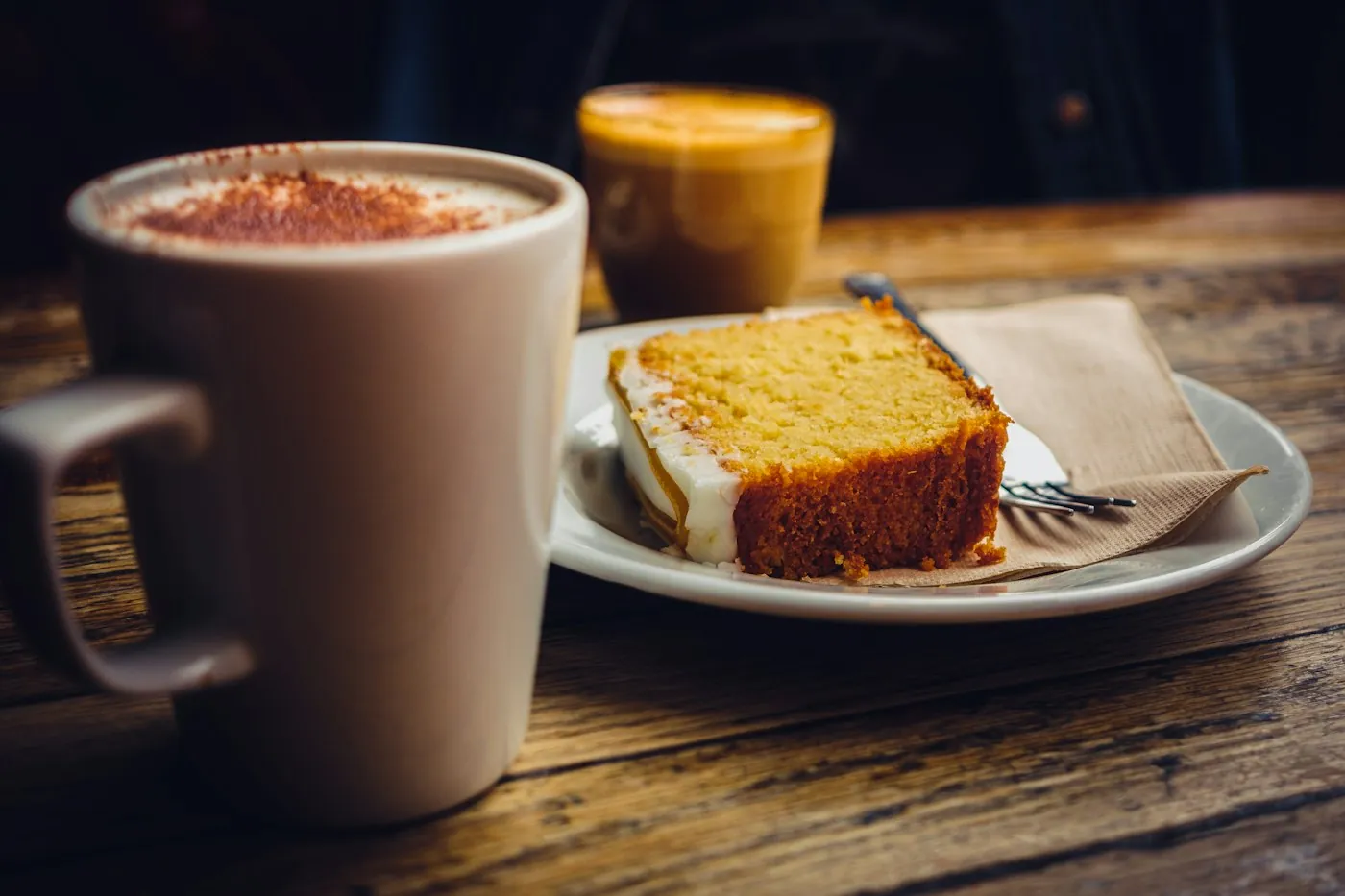A cappuccino and a slice of cake on a wooden table